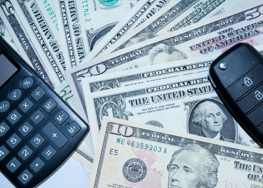 US dollar bills, a calculator, and car keys on a desk
