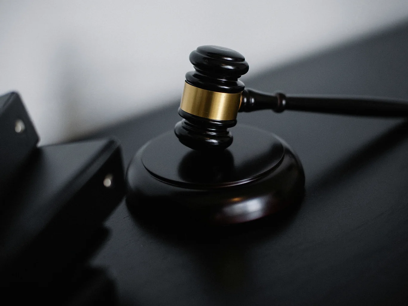A dark wooden gavel with a brass band resting on its sound block, centred on a dark desk against a pale wall