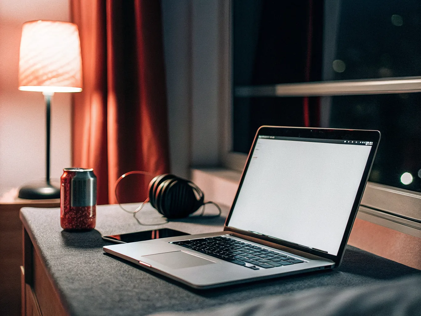 Laptop and phone on an apartment desk at night lit by a warm lamp